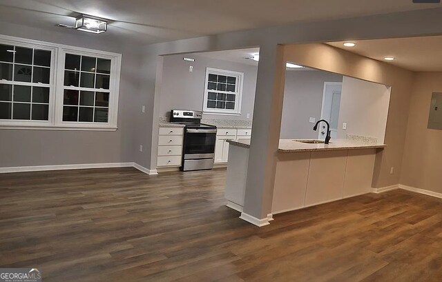 kitchen with dark wood-type flooring, stainless steel range with electric stovetop, a sink, white cabinets, and baseboards