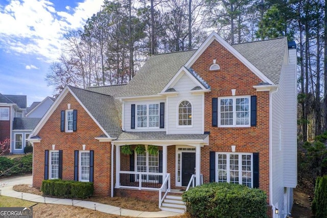 traditional-style home with brick siding, a porch, a chimney, and a shingled roof