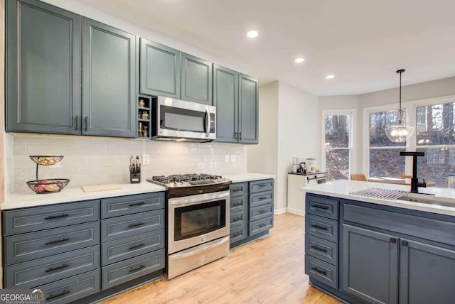 kitchen with a sink, stainless steel appliances, light wood-style floors, light countertops, and decorative backsplash