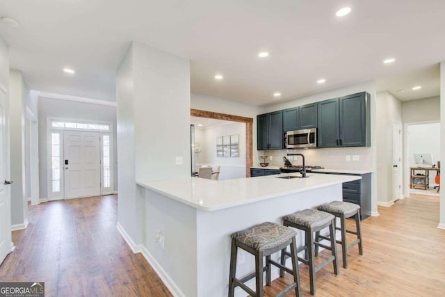 kitchen featuring a breakfast bar, a sink, light countertops, light wood-style floors, and stainless steel microwave