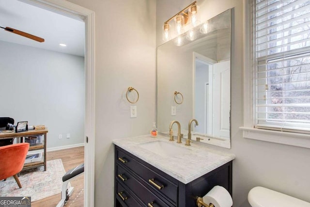 bathroom with vanity, wood finished floors, baseboards, ceiling fan, and toilet