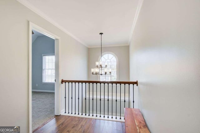 hallway featuring baseboards, a notable chandelier, wood finished floors, and crown molding