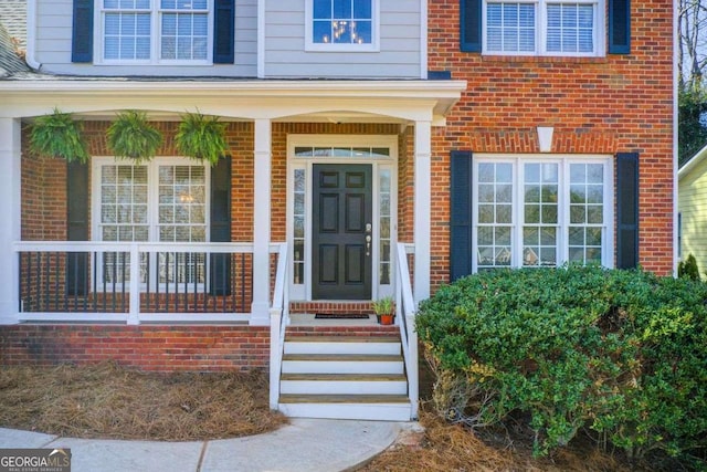 entrance to property featuring a porch and brick siding