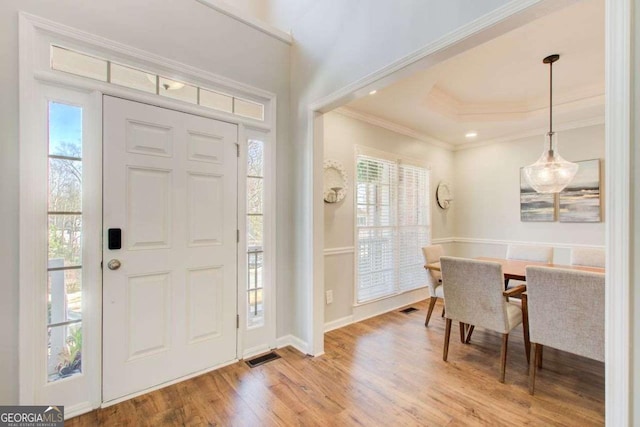 entryway with a raised ceiling, wood finished floors, visible vents, and ornamental molding