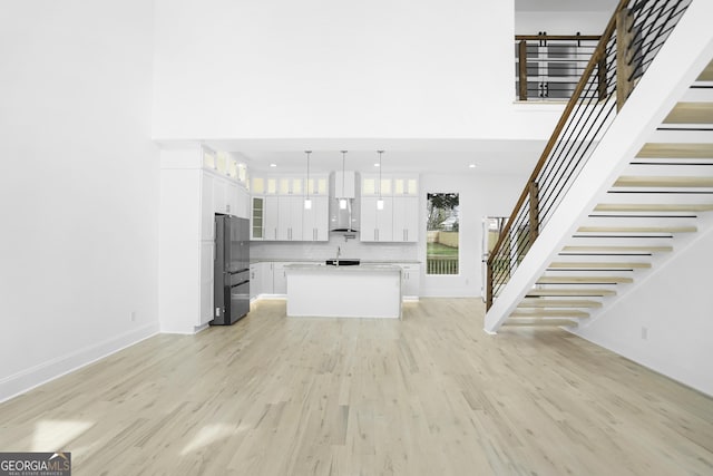 unfurnished living room featuring stairway, baseboards, light wood-style floors, and a towering ceiling