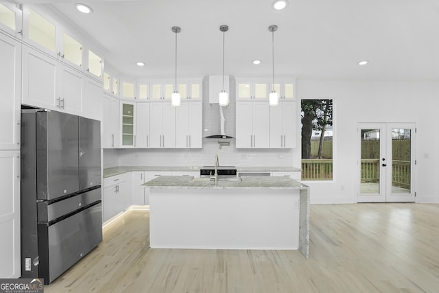 kitchen with light wood finished floors, decorative backsplash, freestanding refrigerator, white cabinetry, and a kitchen island with sink