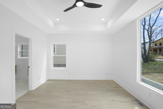 spare room featuring visible vents, baseboards, light wood-type flooring, a tray ceiling, and recessed lighting