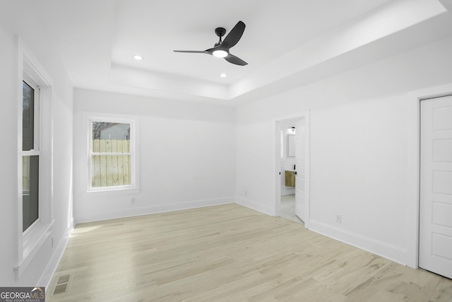 empty room featuring baseboards, visible vents, light wood finished floors, a tray ceiling, and recessed lighting