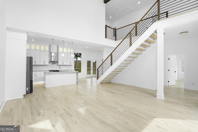 unfurnished living room with stairway, light wood-style flooring, recessed lighting, a sink, and a towering ceiling