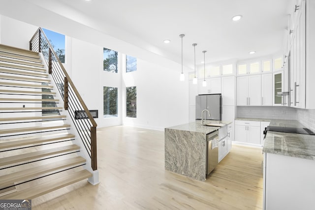 kitchen featuring a sink, stainless steel appliances, light wood-type flooring, and light stone counters