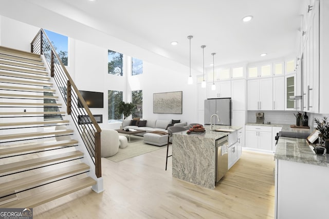 kitchen featuring a sink, light stone counters, light wood-style floors, appliances with stainless steel finishes, and white cabinets