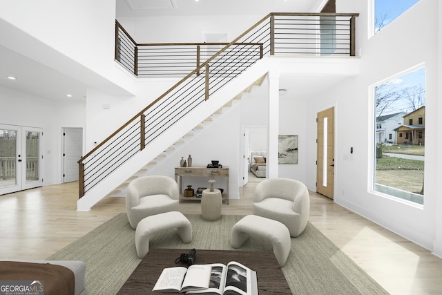 living area with stairway, a high ceiling, french doors, and light wood-type flooring