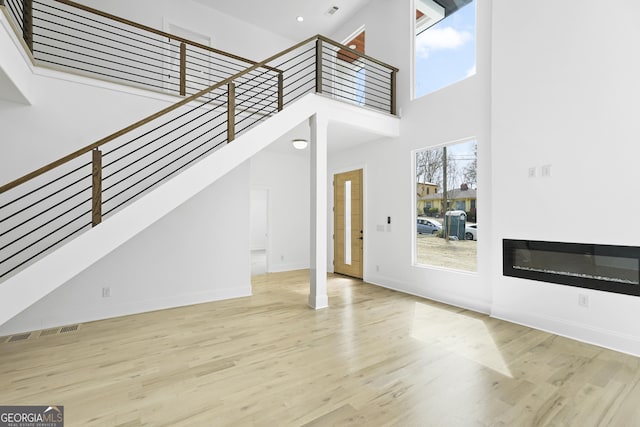 unfurnished living room with a glass covered fireplace, plenty of natural light, wood finished floors, and stairs