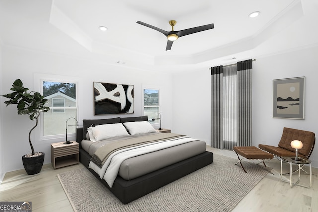 bedroom with a tray ceiling, multiple windows, crown molding, and light wood finished floors