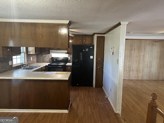 kitchen featuring a peninsula, dark wood-style flooring, a sink, black appliances, and under cabinet range hood