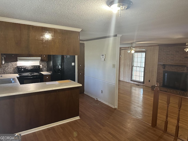 kitchen with under cabinet range hood, light countertops, a peninsula, black appliances, and dark wood-style flooring