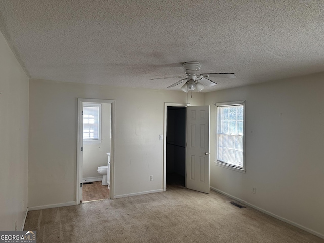 unfurnished bedroom featuring ensuite bath, carpet flooring, baseboards, and visible vents