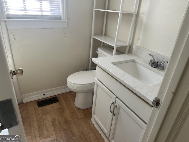 half bath with vanity, wood finished floors, visible vents, baseboards, and toilet