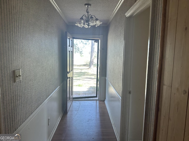 doorway featuring a textured ceiling, wallpapered walls, crown molding, and wood finished floors