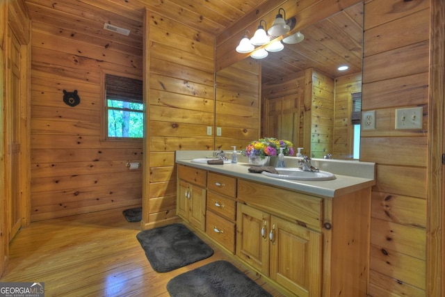 full bath with wooden walls, wood finished floors, double vanity, a sink, and wooden ceiling