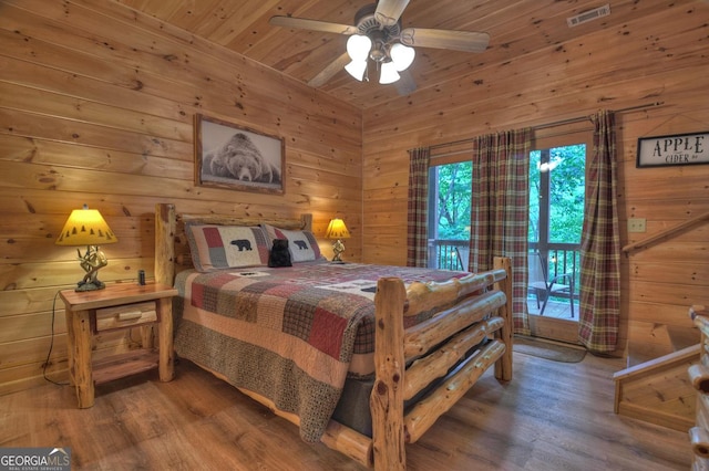 bedroom featuring visible vents, wooden walls, and wood finished floors