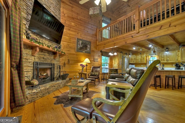 living area featuring light wood-type flooring, a ceiling fan, wooden walls, a stone fireplace, and wooden ceiling