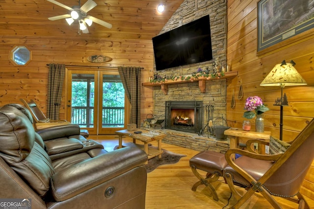 living room featuring a stone fireplace, wooden walls, wood finished floors, and high vaulted ceiling