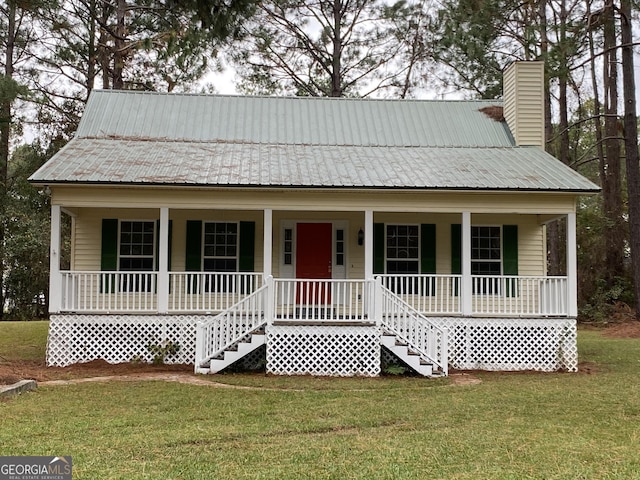 view of front of home with a front lawn, a chimney, covered porch, and metal roof