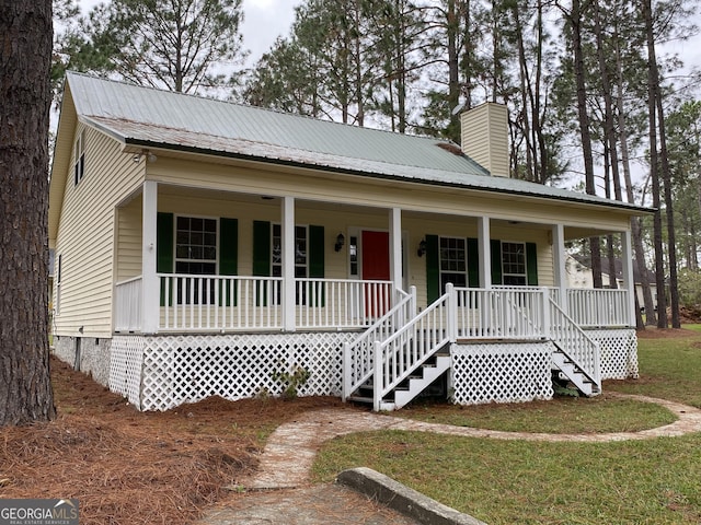 view of front facade featuring a chimney, covered porch, and metal roof