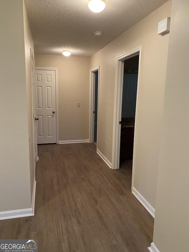 hall with dark wood-style floors, baseboards, and a textured ceiling