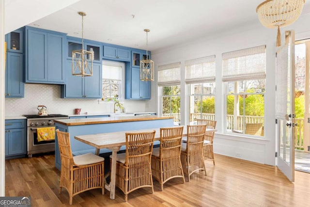 kitchen with blue cabinetry, tasteful backsplash, stainless steel range with gas cooktop, and light wood-style flooring