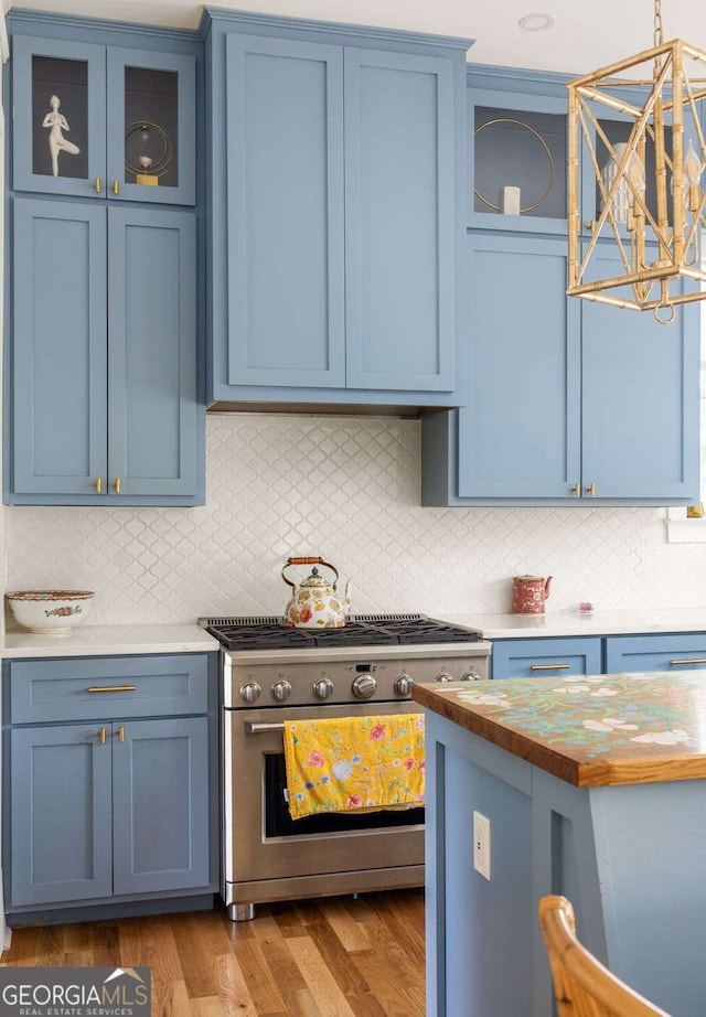 kitchen featuring wood finished floors, stainless steel range with gas stovetop, decorative backsplash, glass insert cabinets, and blue cabinets