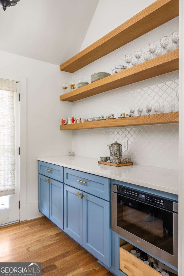 bar featuring tasteful backsplash, light wood-style flooring, and vaulted ceiling