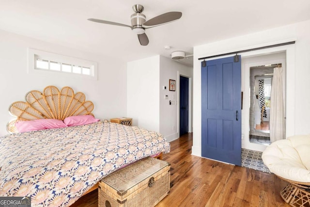 bedroom with ceiling fan, a barn door, baseboards, and wood finished floors