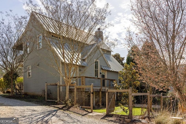 exterior space featuring a wooden deck, metal roof, a chimney, and a standing seam roof