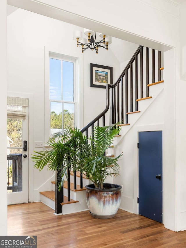 staircase featuring wood finished floors, a wealth of natural light, and a chandelier