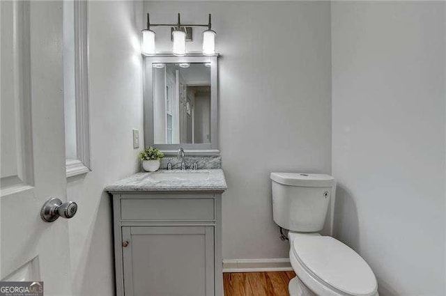 half bathroom with toilet, vanity, baseboards, and wood finished floors