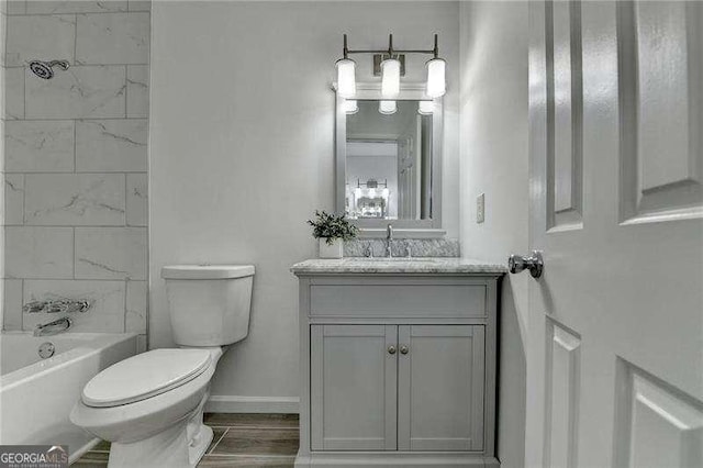 bathroom with vanity, wood finished floors, baseboards,  shower combination, and toilet