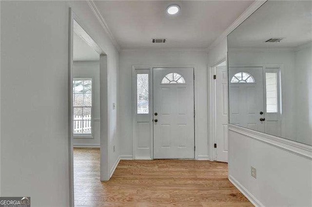 foyer entrance featuring crown molding, light wood-style flooring, and visible vents