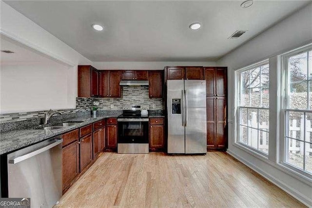 kitchen featuring light wood-style flooring, a sink, under cabinet range hood, stainless steel appliances, and decorative backsplash