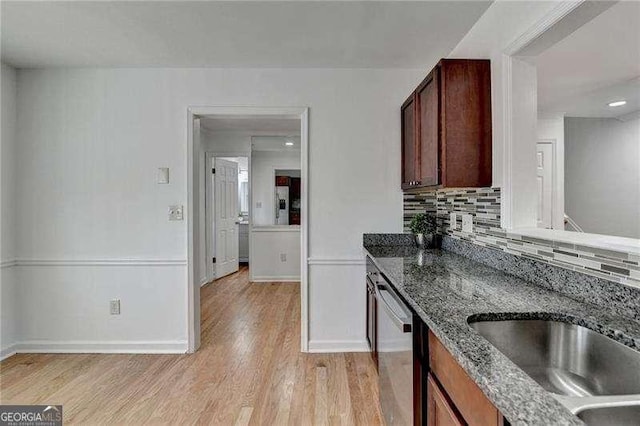 kitchen with light wood-type flooring, a sink, dark stone counters, decorative backsplash, and dishwasher