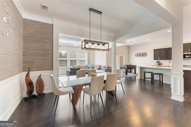 dining room featuring visible vents, crown molding, dark wood-type flooring, wainscoting, and ornate columns