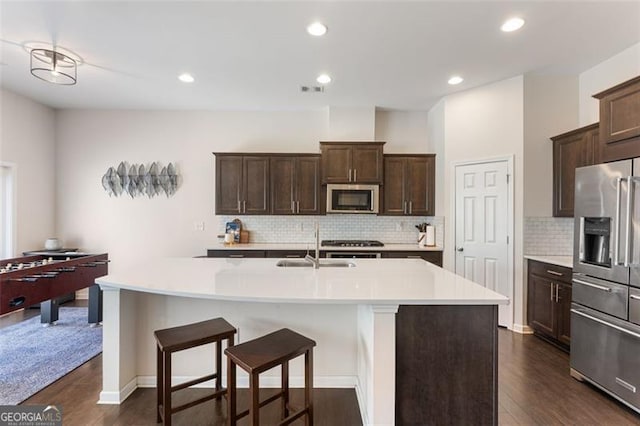 kitchen with a kitchen island with sink, stainless steel appliances, dark wood-type flooring, light countertops, and dark brown cabinetry