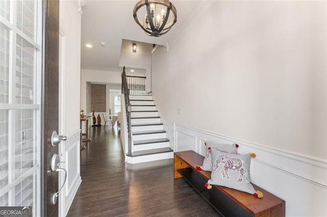 foyer entrance featuring a wainscoted wall, dark wood finished floors, stairs, a decorative wall, and a chandelier