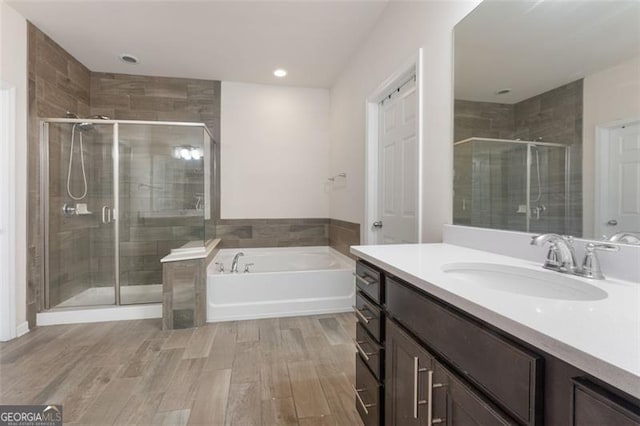 full bath with a shower stall, vanity, a garden tub, and wood finished floors