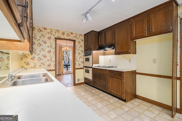 kitchen with light floors, double oven, wallpapered walls, and a sink