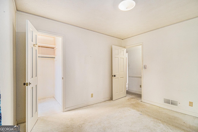 unfurnished bedroom with visible vents, a walk in closet, a closet, baseboards, and light colored carpet