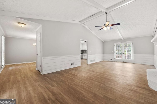 unfurnished living room featuring a ceiling fan, a textured ceiling, wood finished floors, wainscoting, and vaulted ceiling with beams