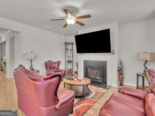 living area with a glass covered fireplace, baseboards, a ceiling fan, and wood finished floors