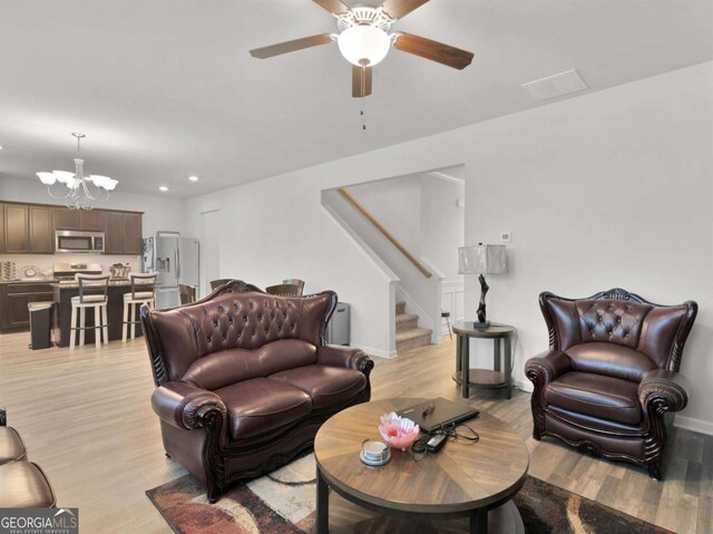 living room featuring light wood finished floors, baseboards, stairs, recessed lighting, and ceiling fan with notable chandelier